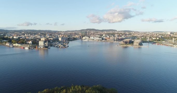 Cinema 4K drone shot with backward tilt motion revealing the forest on hoved&oslash;ya island with a background view of Bj&oslash;rvika, with the Lambda Munch Museum and Oslo Opera House in autumn, in Oslo Norway.