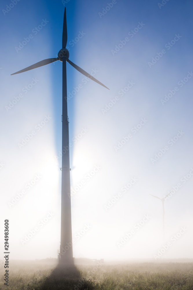 Wall mural a wind turbine in the early morning in fog and backlight. concept: modern energy production