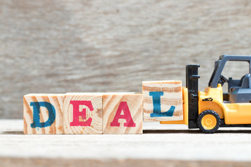 Toy forklift hold letter block l to complete word deal on wood background