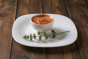 A sprig of fragrant grass and red and white sauce in a white bowl on a wooden table. Vegetarian sauce.