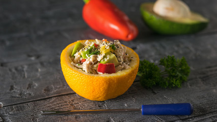 Half an orange with salad, pepper and avocado with fork on wooden table.