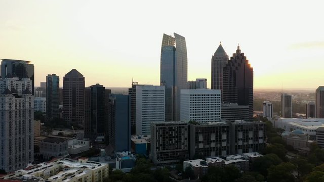 4K Ariel Drone Shot Passing Around Beautiful Skyline Buildings In Charlotte, North Carolina. USA. Golden Sun Shining Through Gaps Of Buildings. Area Covered With Trees. Golden Yellow Sky.