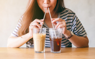 Closeup image of a beautiful asian woman drinking two glasses of iced coffee with stainless steel straws at the same time