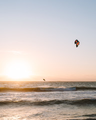 Fototapeta na wymiar Man kitesurfing at Scarborough Beach as the sun sets over the ocean in the distance. 