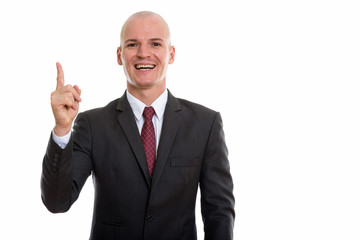 Studio shot of young happy bald businessman smiling while pointi