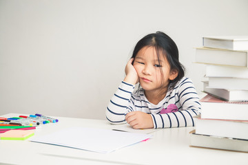 A girl studying at an elementary school level is tired of studying, with books full of her desk, she doesn't feel fun. Educational concepts for young children