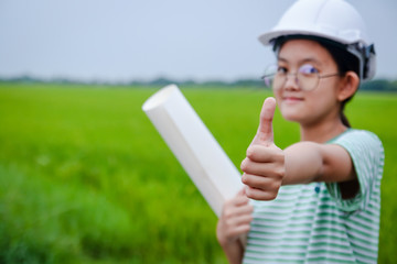 A young Asian girl engineer wearing a white safety hat holding a paper roll.