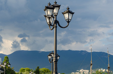 Lamppost by the sea on the background of the masts of the ship and the mountains.