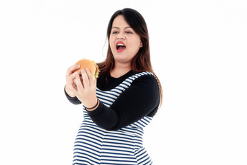 A young fat woman is eating a hamburger in her hand. She is smiling and happy to eat the food she likes. She is hungry. Healthy concept. Isolated on a white background.