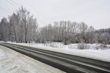 Snowy winter road in pine and birch forest.The Northern part of Russia