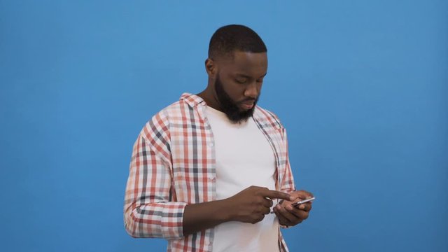 Portrait of handsome excited cheerful joyful delightful curious guy wearing casual sending and getting messages to his lover isolated against blue background. Using phone. 4K