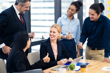 Caucasian business working woman sitting in meeting room receiving complements and congratulations from colleague with various nationalities by giving her thumb ups. The girl feeling happy with smile.