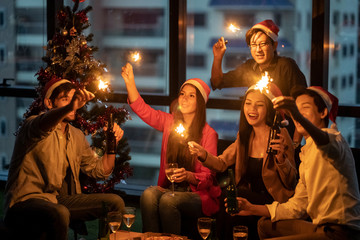 Group of diversity people having great Christmas party in working office together at night. They celebrate with beer and holding sparklers feeling happy and enjoy laughing. Xmas new year party concept