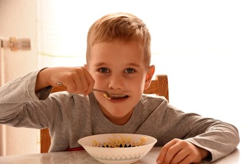  boy sits on a chair at the table and eats pasta from a plate