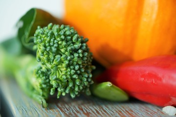 fresh broccoli and red pepper and by orange pumpkin on wooden surface