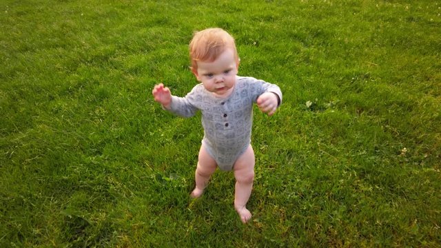 Happy toddler takes first steps unassisted without help in grass field. Determined face shows focus as he carefully walks toward camera proud of his accomplishment. unsteady. developing coordination