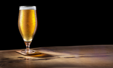 Glass of light beer on the bar counter on a black background.