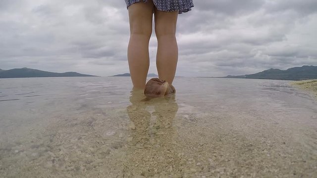 A slow motion video of a coconut drifting slowly next to a girl standing on the waters edge