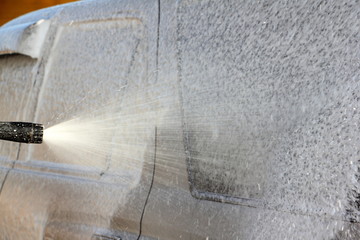 Spraying of white shampoo on the side surface of the grey SUV vehicle from a foaming gun at the car wash