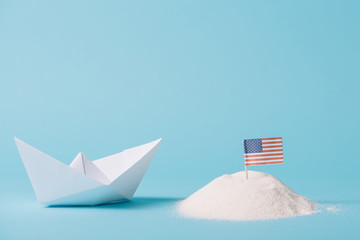 paper boat near American national flag in white sand on blue background