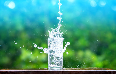Drink water pouring in to glass over sunlight and natural green background.Select focus blurred background.