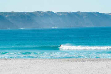Lone man surfing a wave on a secluded beach in Albany with te backdrop of beautiful mountains over...