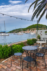 A beautiful Mediterranean beach bar terrace empty after rain decorated with flowers, palm trees and lights with a view of sailing boats in the port of Vis , Vis island, Croatia, Europe. Summer travel