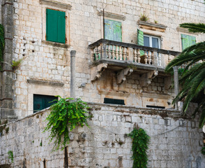 Fototapeta na wymiar Beautiful details on an old stone house with a beautiful balcony and with green doors and green wooden shutters and overgrown walls, mediterranean architecture, Vis island, Croatia, Europe