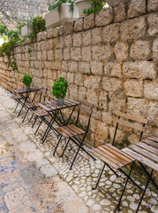 Fototapeta na wymiar Chairs and tables leaning against an old stone wall in a narrow typical mediterranean stone street, empty after rain. Vis island, Croatia, Europe. 