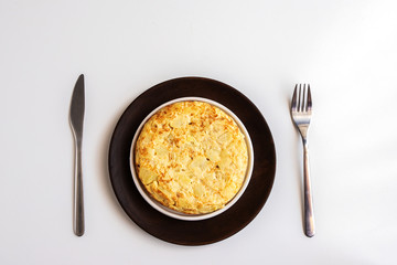 Top view  of Tortilla, Spanish omelette made with eggs and potatoes on the plate with cutlery at white background. Traditional Spanish tapas
