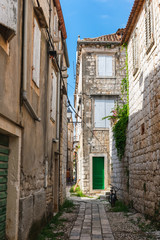 Beautiful view of a narrow Mediterranean street with stone houses with green doors and wooden shutters and mediterranean plants. Vis island, Croatia, Europe. Summer and travel concept.