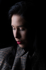 Portrait of a young woman in black and white (LowKey) in front of a black background, she freezes and holds up her coat collar with her hands..