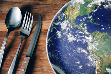 The planet Earth plate with a fork and knife on a wooden background. World hunger concept. Feed the world. - obrazy, fototapety, plakaty
