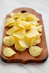 Tasty potato chips with salt on a rustic wooden board, low angle view. Close-up.
