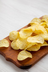 Yellow potato chips with salt on a rustic wooden board, low angle view. Space for text.