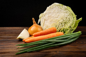 Fresh cabbage, green onion and carrot on dark wooden background.