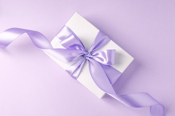 Craft gift box on a lilac background, decorated with a textured bow and feathers, creating a romantic luxury atmosphere. For birthday, anniversary presents, gift post cards.