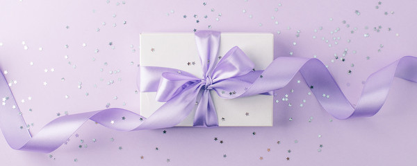 Craft gift box on a lilac background, decorated with a textured bow and feathers, creating a romantic luxury atmosphere. For birthday, anniversary presents, gift post cards.