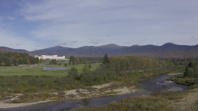 Aerial 4K HDR video of Mount Washington in White Mountains, New Hampshire during fall day. Drone moving forwards with golf course and old hotel in foreground.