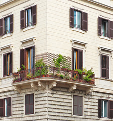 Corner of a house with a balcony on which there are a lot of potted green plants and ivy on trellis