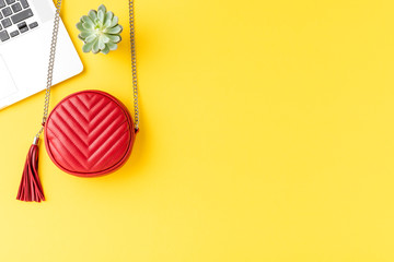 Fashion background with red woman’s purse with laptop and small green succulent on yellow desktop