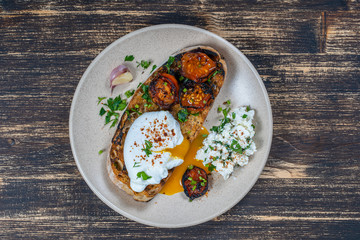 Poached egg on a piece of bread with fried red tomato, garlic and cottage cheese on a plate, close up