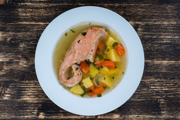 Fresh salmon fish soup with carrots and potatoes in a white plate, close up