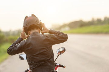 Handsome motorcyclist wear leather jacket and holding helmet on the road