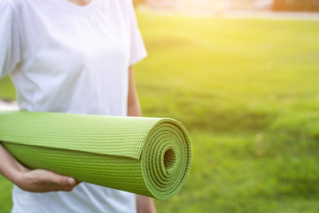 Pretty asian holding green yoga mat and prepare for doing yoga exercises in the park.