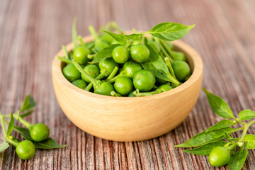 Green circle chilli or cherry peppers in wood bowl on table plank background