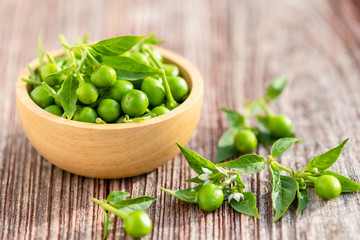 Green circle chilli or cherry peppers in wood bowl on table plank background
