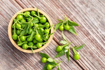 Green circle chilli or cherry peppers in wood bowl on table plank background