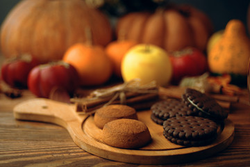 Cookies with pumpkins and apples on the table. Chocolate chip cookies with pumpkins on an old wooden table with autumn crops on a blurred background.
