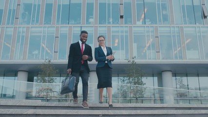 Two employees, delegates or lawyers walk on stairs from business center. Colleagues finished work day in their modern glass office. Man and woman in formal suits